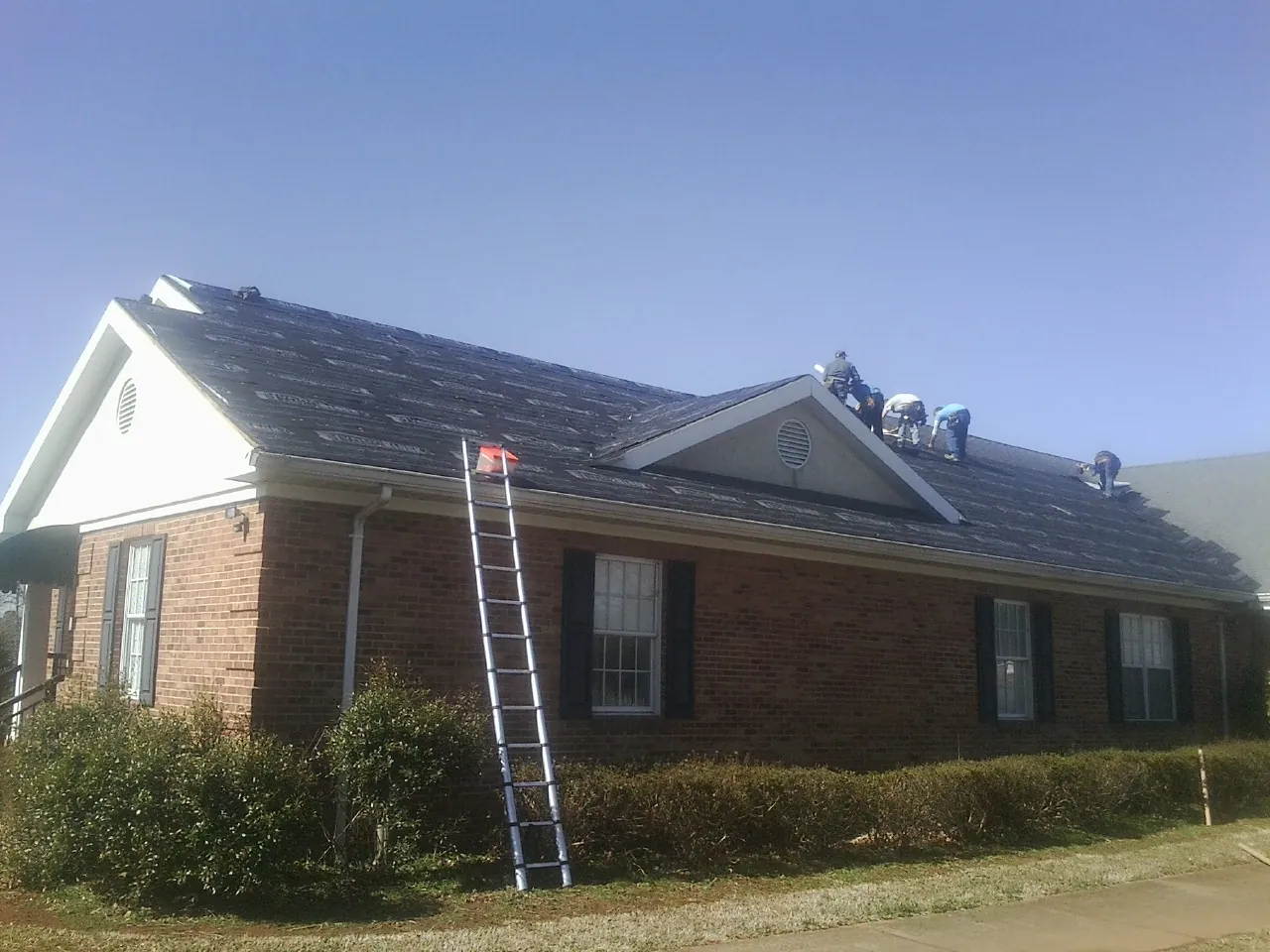 Crew tearing shingles off a brick ranch roof with a ladder set — Emergency Roof Repair work by our crew in Bruceton