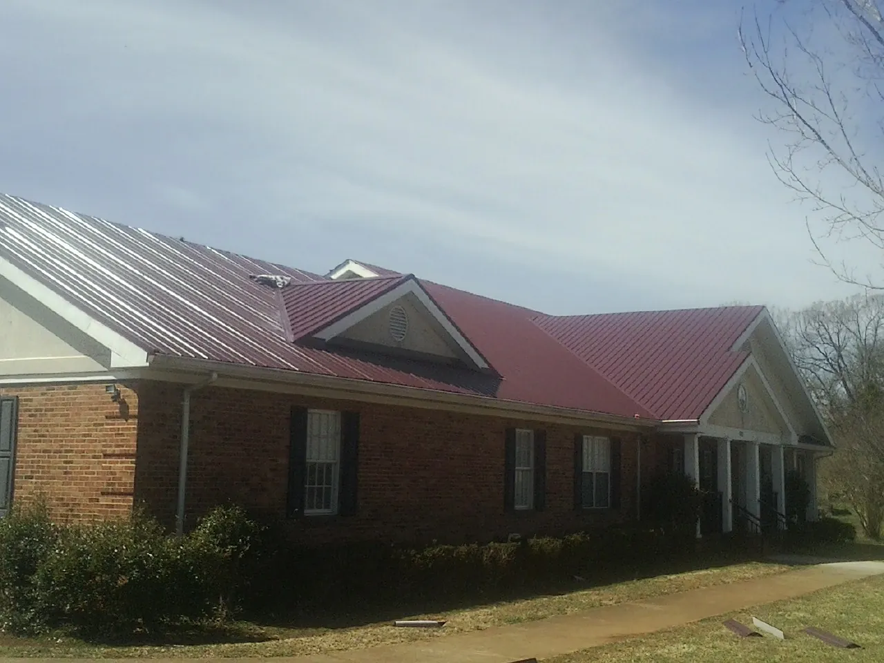 Red metal roof with gabled entries on a long brick building, from a Hail Damage Roof Repair job in Bruceton