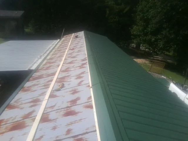 Old rusted panels beside newly installed green metal roofing — Wind Damage Roof Repair by Roofing Brothers in Bruceton