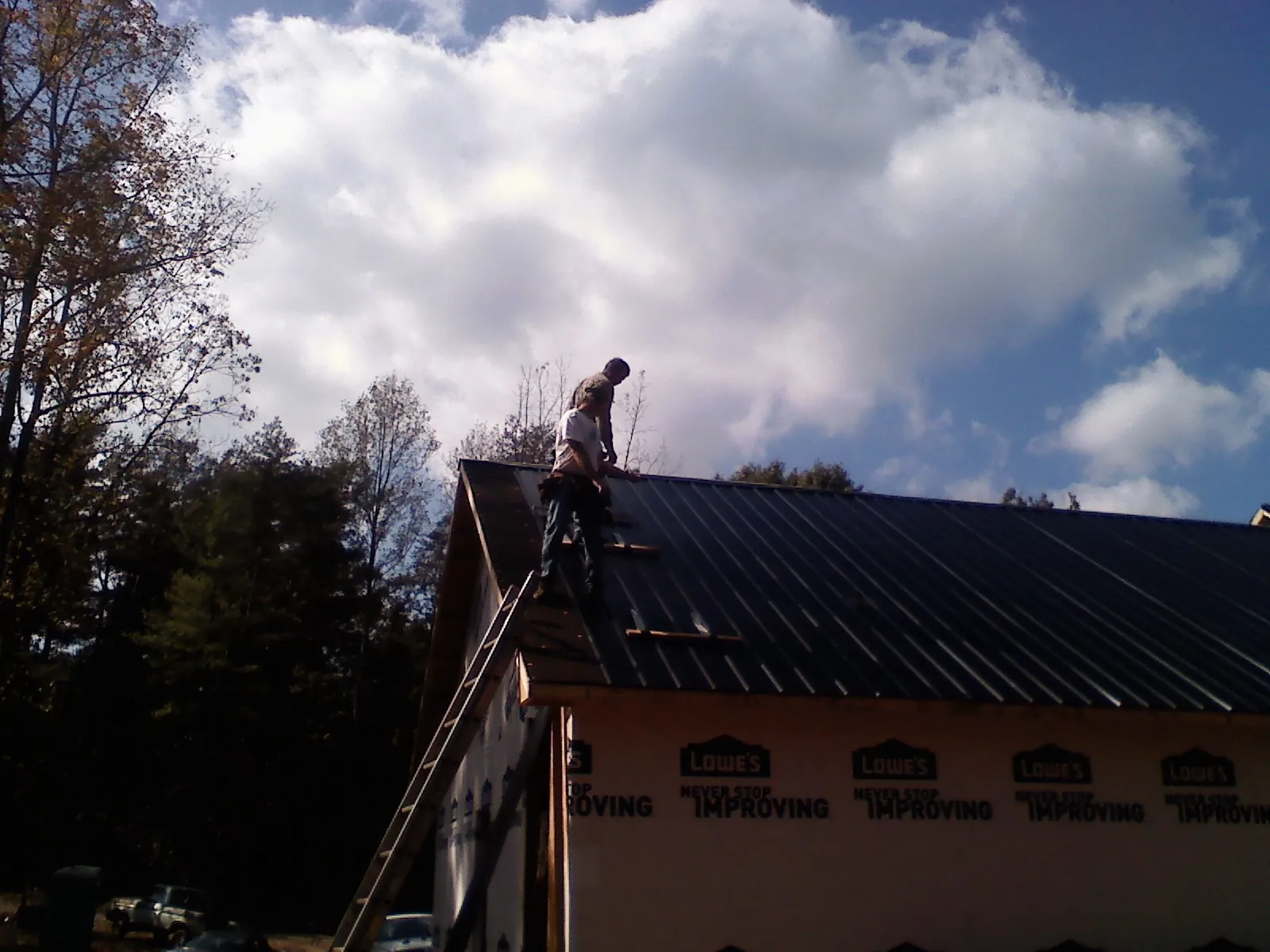 Roofer fastening dark metal panels high against a cloudy sky, from a Roof Inspection job in Bruceton