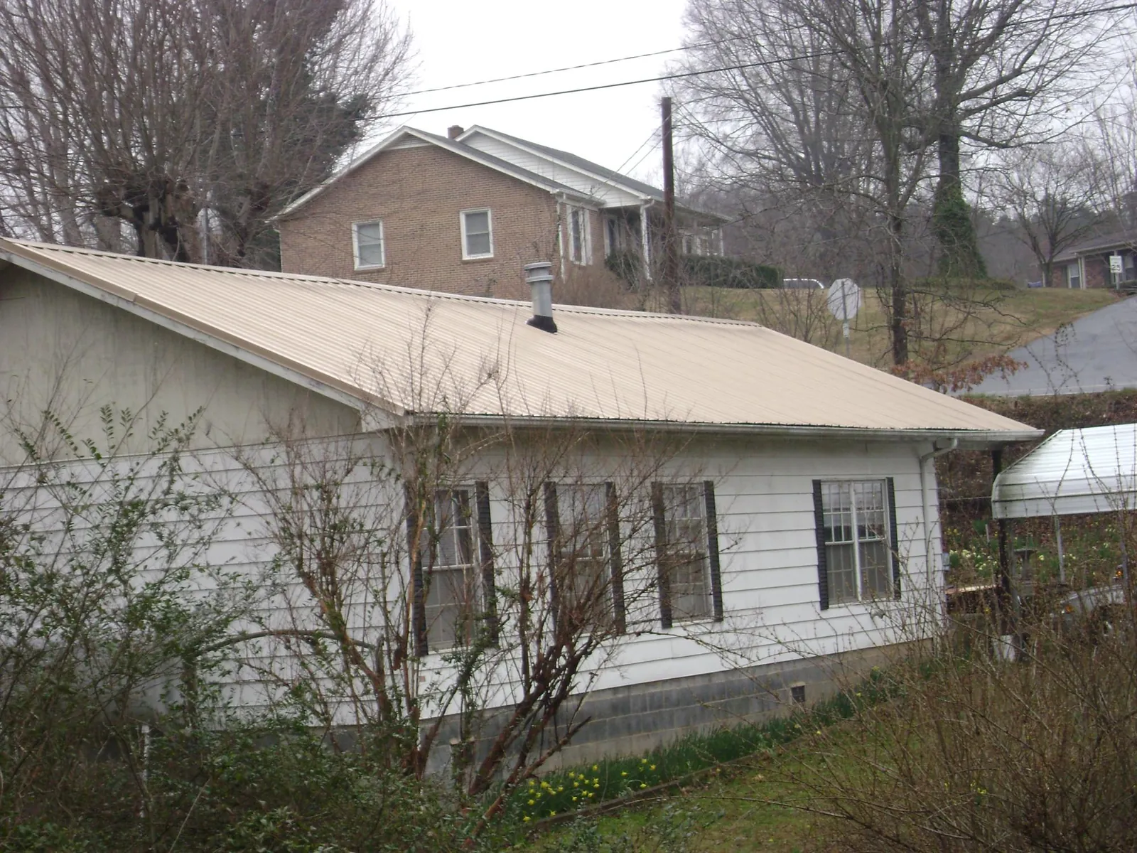 Tan metal roof on a white sided house set into a hillside — Commercial Roofing by Roofing Brothers in Bruceton
