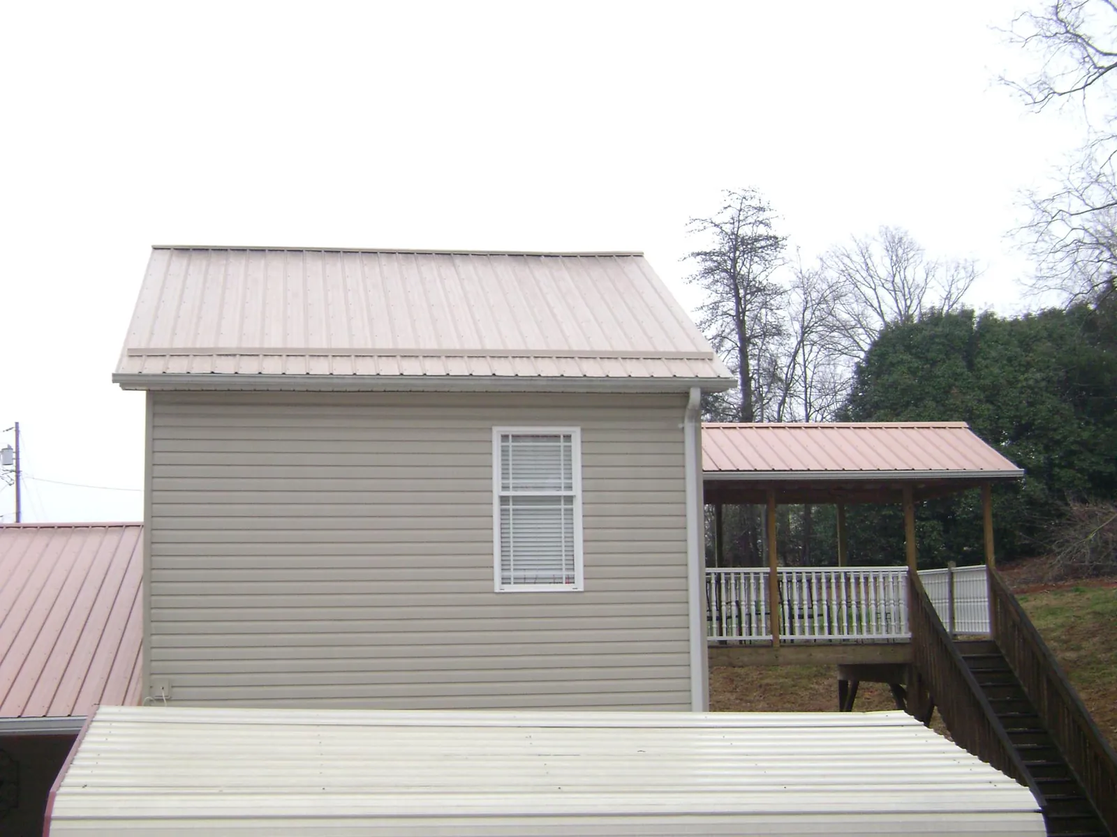 Tan metal roofs on a two story addition and attached porch, from a Roof Replacement job in Bruceton